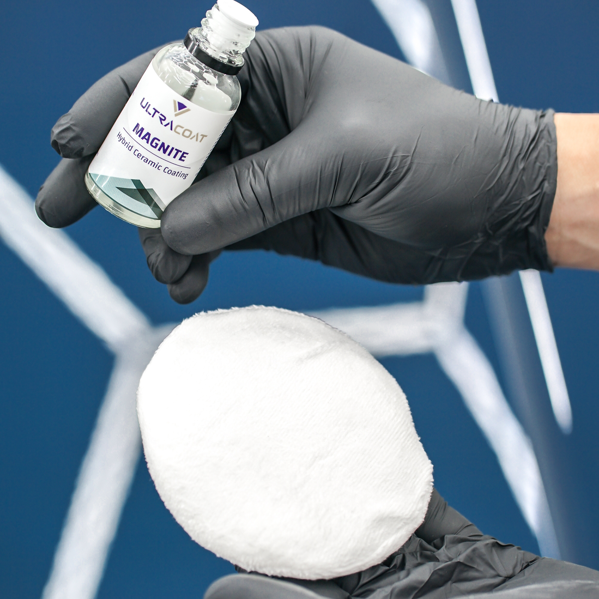 Gloved hand holding the Ultracoat Magnite bottle above a white microfibre applicator pad