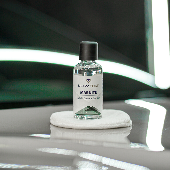 Ultracoat Magnite ceramic coating bottle standing on a white microfibre applicator pad against a dark studio backdrop