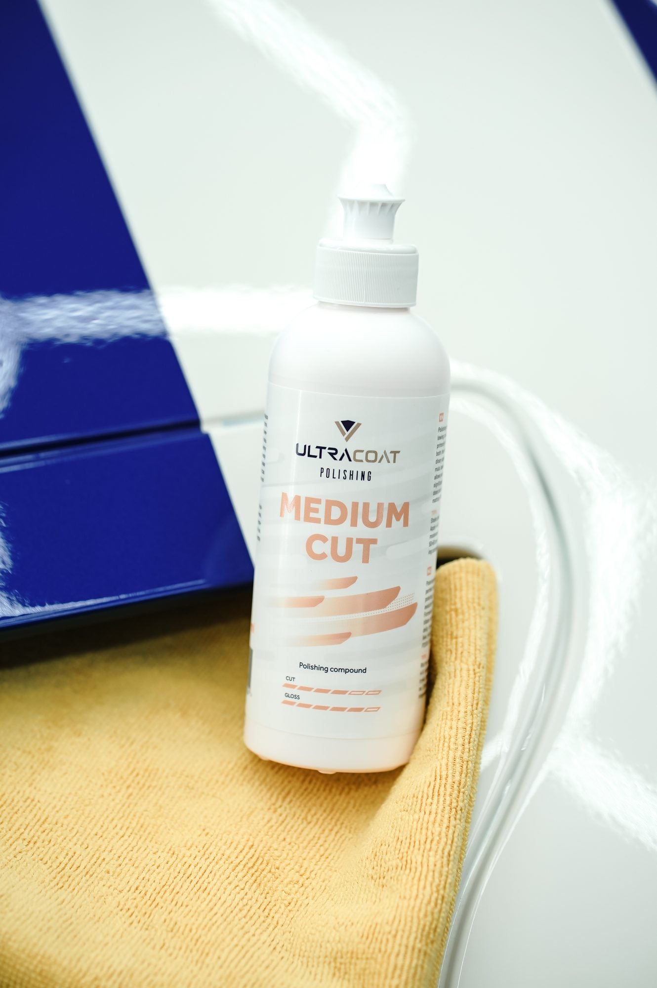 Ultracoat Polishing Medium Cut bottle with orange microfibre cloth on a white vehicle with blue accent