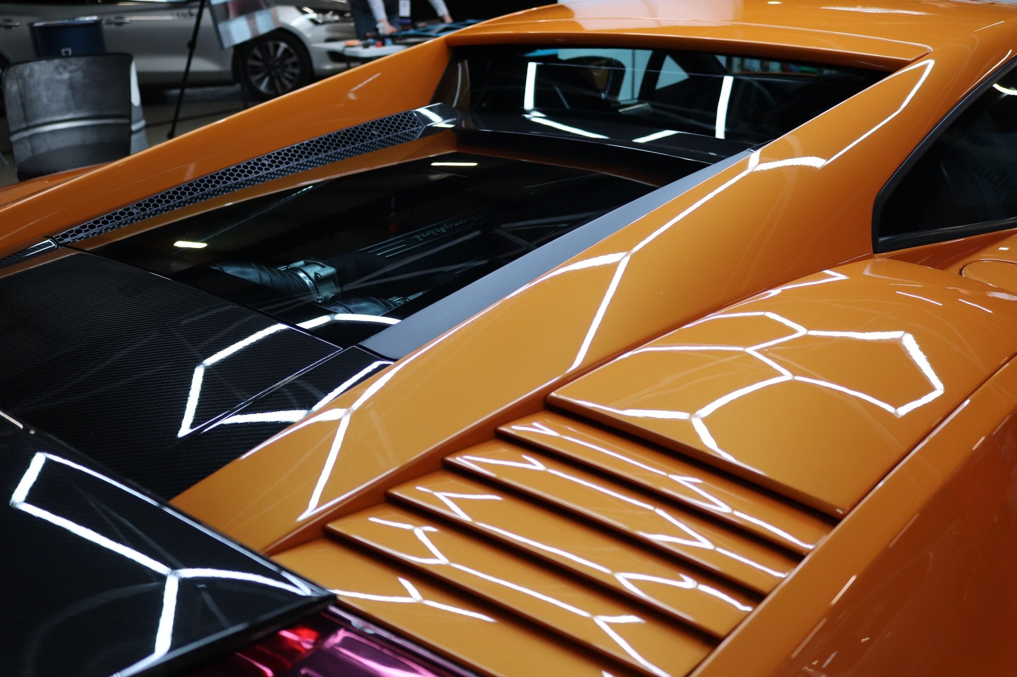 Sharp reflected light across glossy orange paintwork, engine cover detail