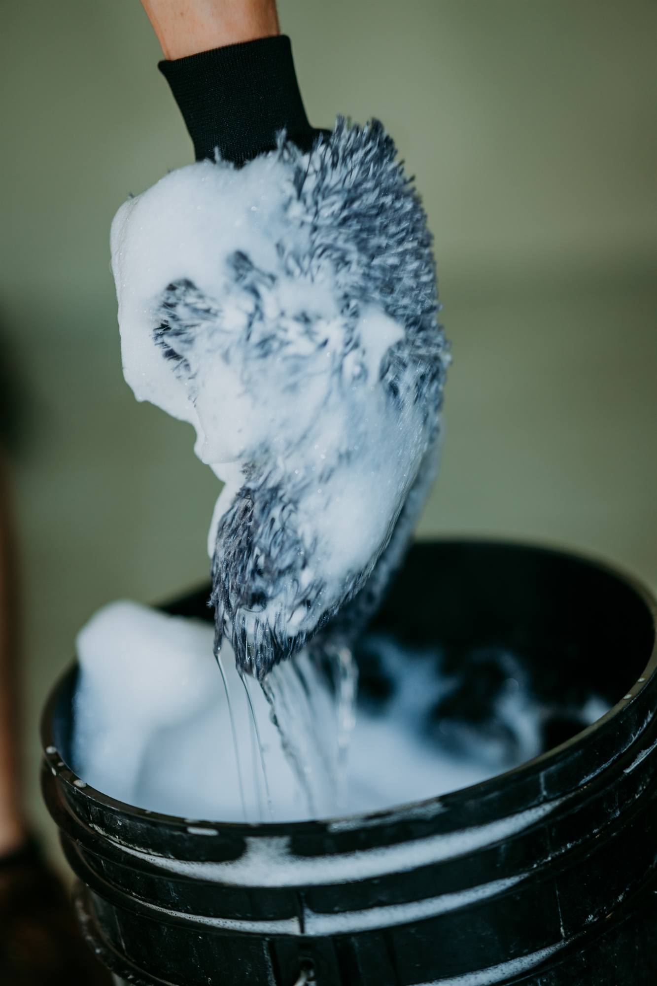Wash mitt dripping with suds over a bucket