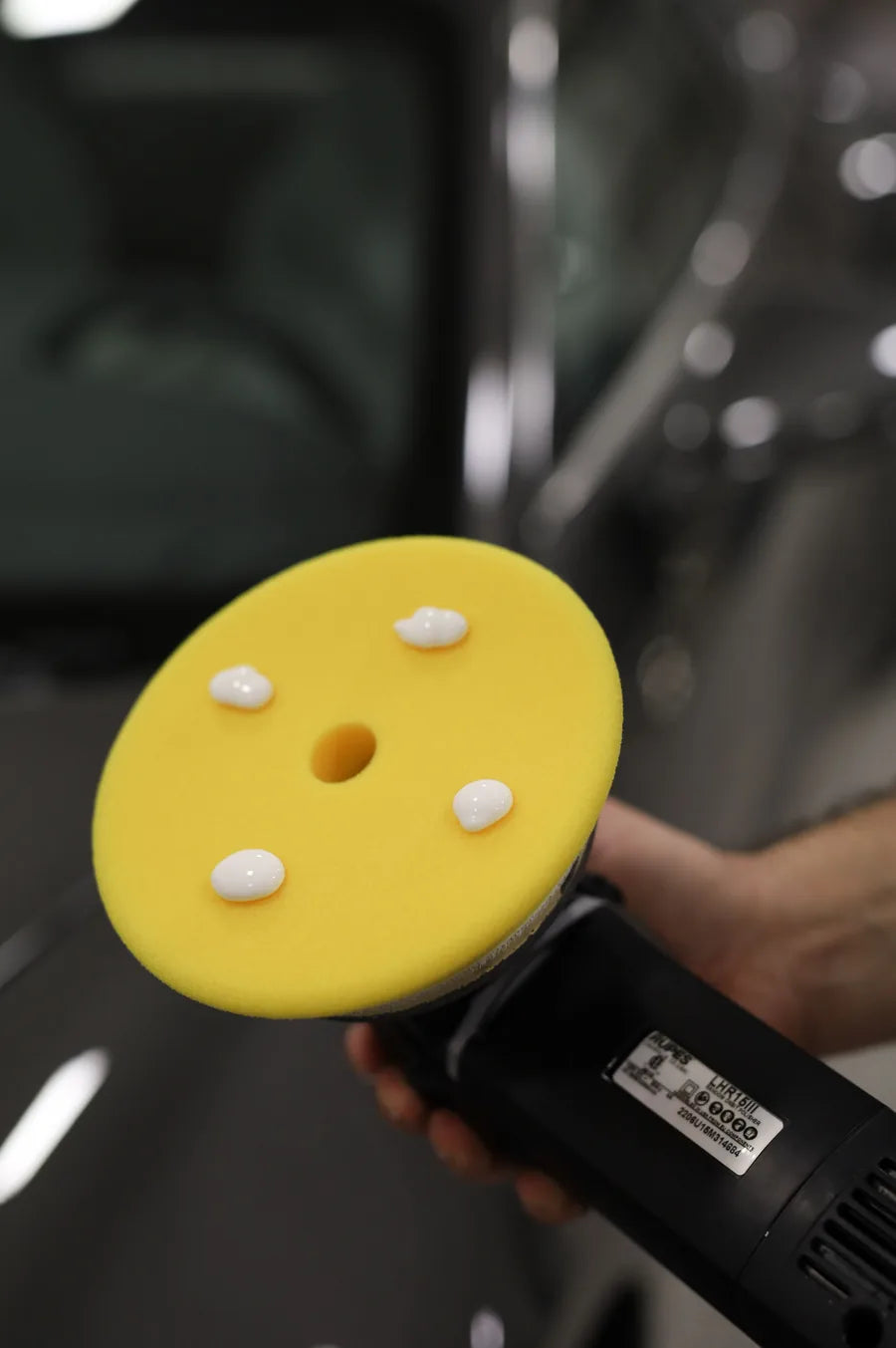 Yellow foam polishing pad on a dual-action machine polisher, held against a vehicle's paintwork